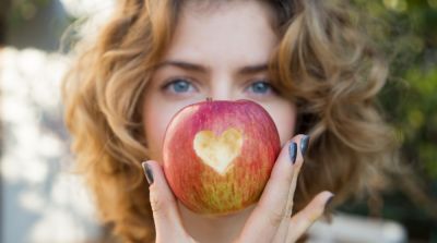 healthy eating - young woman holds a red apple in front of her face with a heart cut out in it. selective focus. proper vitamin nutrition. love concept. health care, cardiology